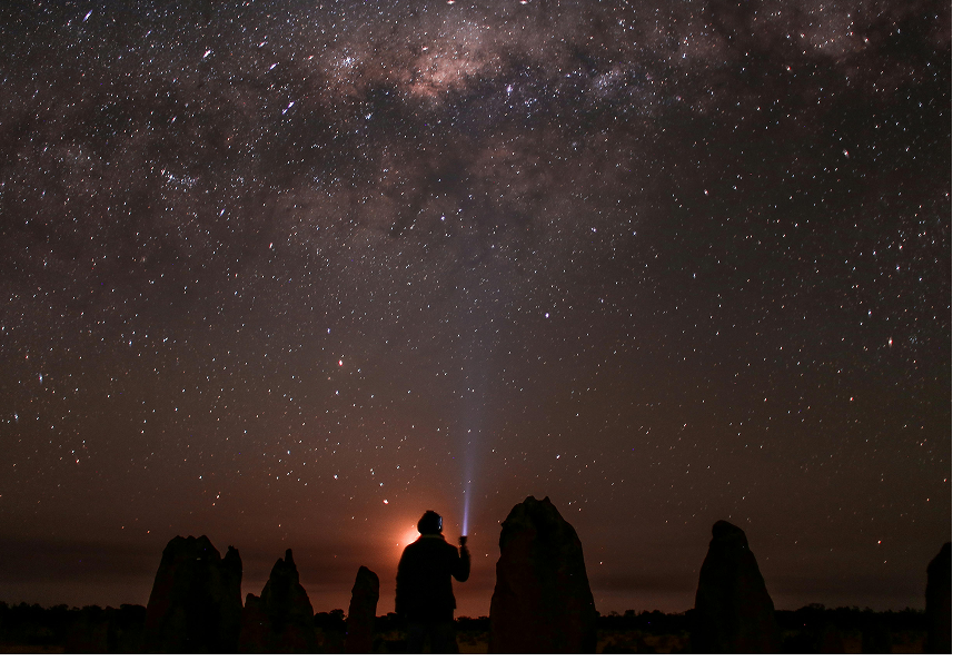 Silhouette of a person with a flashlight looking up at a starry sky